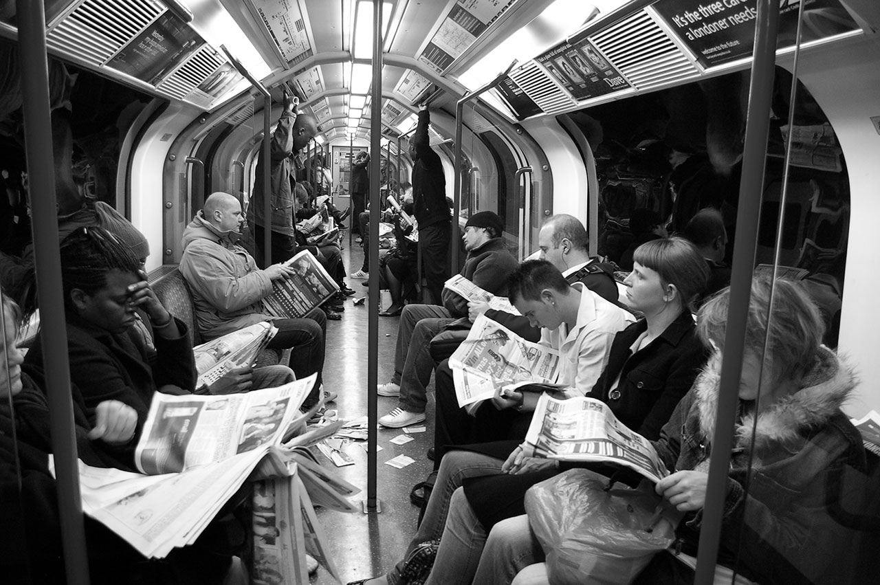 Sanomalehtiä lukevia ihmisiä metrossa.